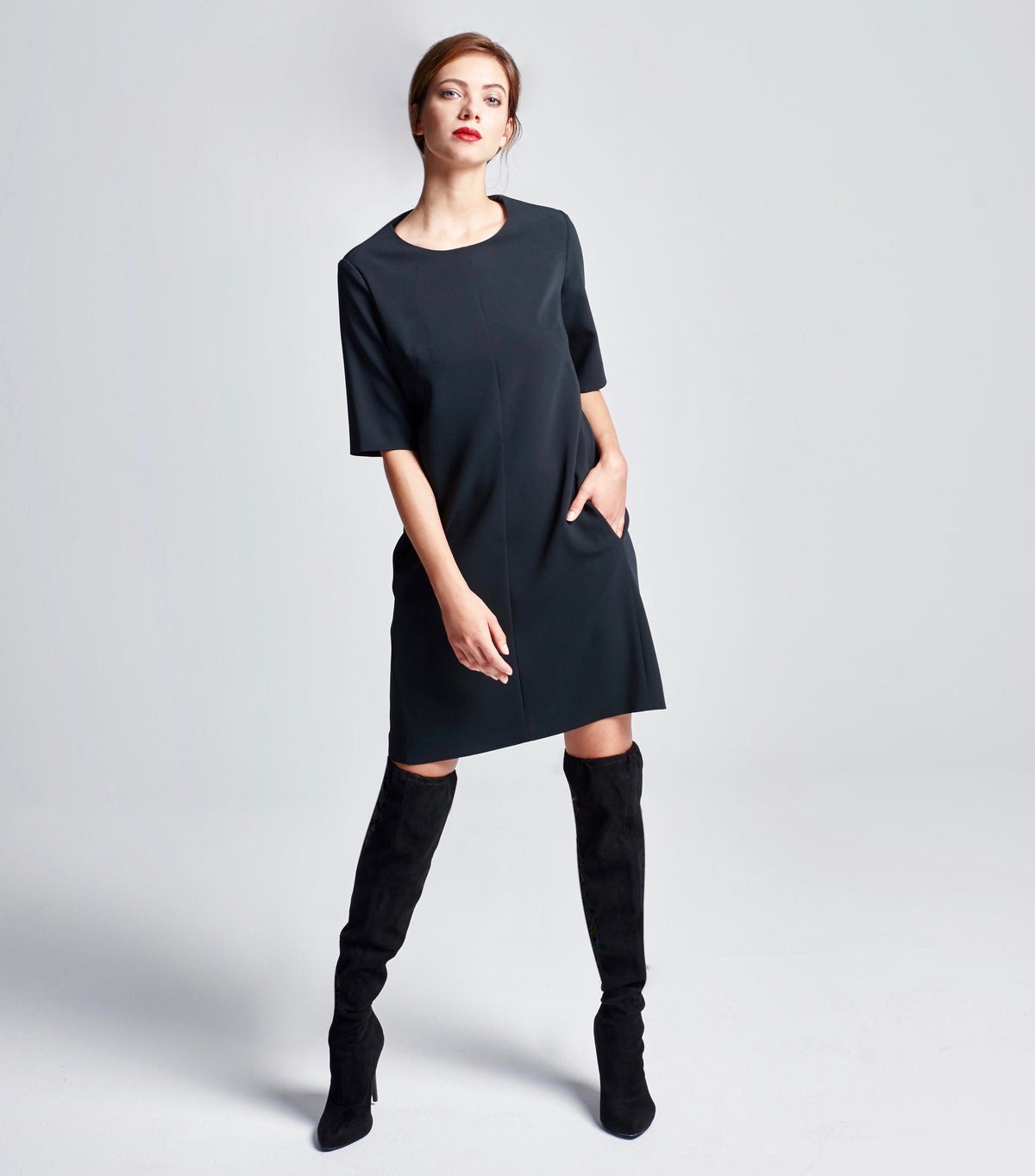 Schwarzes Multiplyfashion Shiftkleid mit 3/4 Arm, knielangem Rock und Eingriffstaschen. Das Model trägt den Look mit Wildlederstiefeln.
